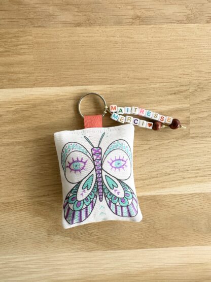 porte-clés colorié du kit pour fabriquer son cadeau Merci maîtresse merci maître ou ATSEM avec un porte-clés papillon en tissu à colorier, des stylos gel et des perles lettre alphabet imaginé par Anne Da Cunha-Guillegault en exclusivité pour la marque An'imato