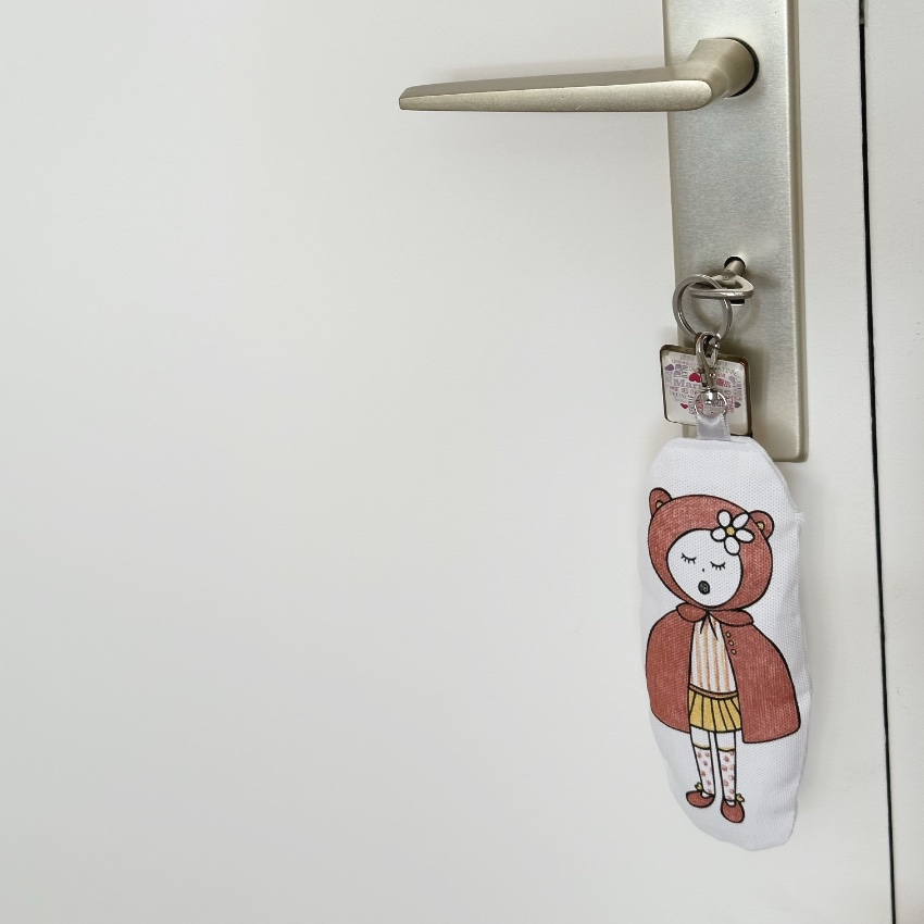 Porte-clés accroché sur une porte en tissu motif chaperon colorié en rouge imaginé par Anne Da Cunha-Guillegault en exclusivité pour la marque An'imato