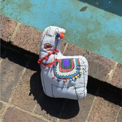Coussin lama Raoul au bord de l'eau colorié aux feutres à l'eau avec pompon et guirlande de pompons du kit coussin à personnalisé imaginé par Anne Da Cunha-Guillegault en exclusivité pour la marque An'imato sert de doudou À emporter partout avec votre enfant