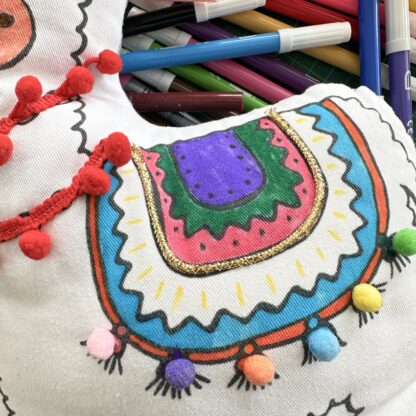 Zoom sur la selle coloriée du coussin lama Raoul au bord de l'eau (colorié aux feutres à l'eau avec pompon et guirlande de pompons) du kit coussin à personnalisé imaginé par Anne Da Cunha-Guillegault en exclusivité pour la marque An'imato sert de doudou À emporter partout avec votre enfant