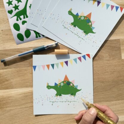 Pochette 5 invitations anniversaire thème dinosaure avec ballons gommettes, stylo gel et colles à paillette carte et gommettes imaginées par Anne Da Cunha-Guillegault en exclusivité pour la marque An'imato