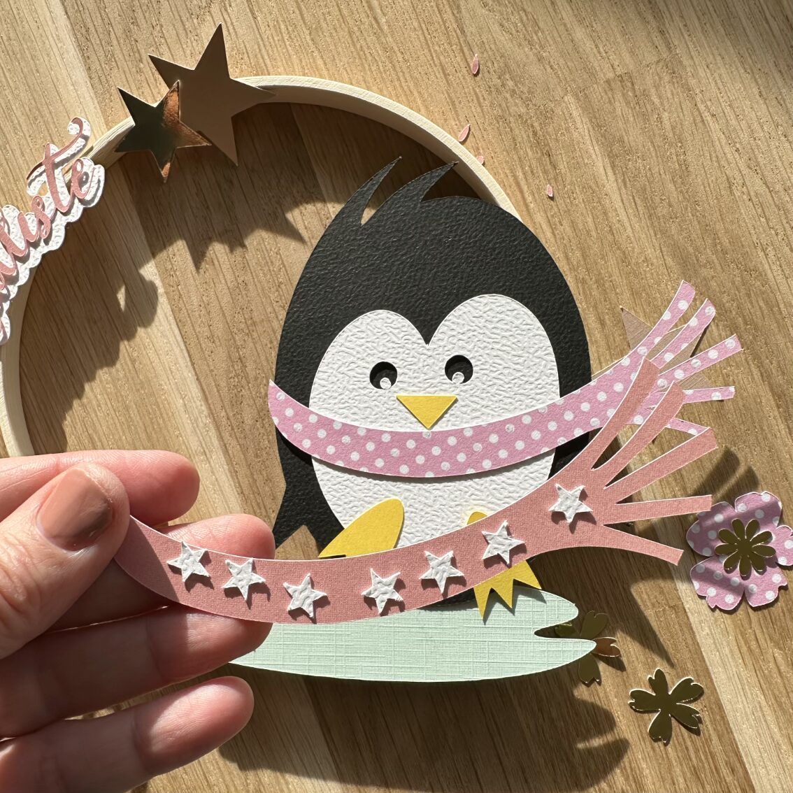Déco unique pour une naissance ou un anniversaire | Cercle décoratif personnalisé avec un pingouin sur la glace et un prénom en papiers découpés | Détail de l'écharpe | Design Anne Da Cunha-Guillegault en exclusivité pour la marque An'imato